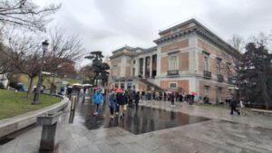 Acceso principal al Museo del Prado con visitantes haciendo cola en un día lluvioso en Madrid.