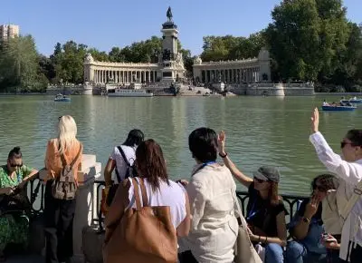 Un grupo de turistas observa el Monumento a Alfonso XII desde la orilla del Estanque Grande del Retiro mientras una guía hace indicaciones.