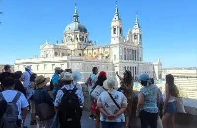 Un grupo de turistas observa y fotografía la Catedral de la Almudena desde un mirador cercano en un día despejado en Madrid.